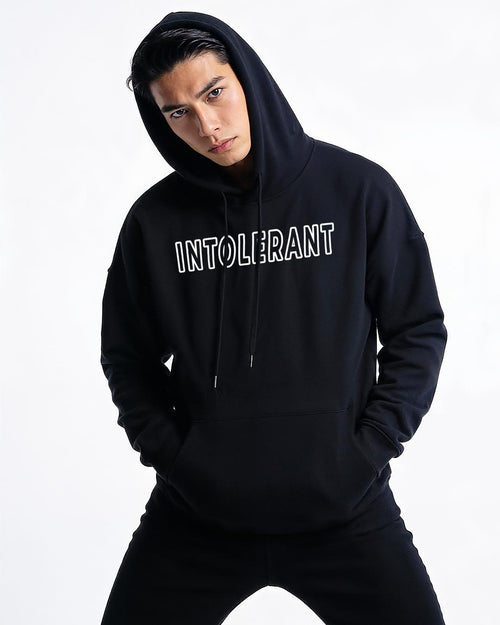 Junger Mann präsentiert den schwarzen INTOLERANT Classic Hoodie in souveräner Pose – klassisch-modernes Design für einen starken Auftritt.