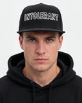 Elegannter Mann trägt die schwarze INTOLERANT Essential Snapback Cap – klarer und sportlicher Look mit markantem weißem Stick.